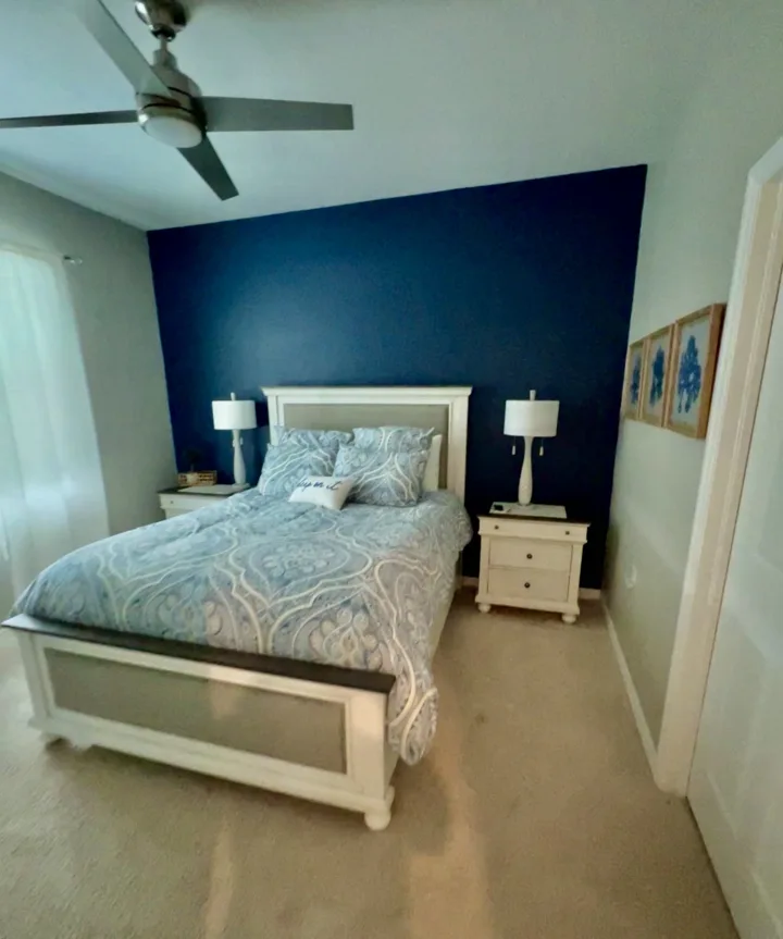 Bedroom with a deep blue accent wall, white furnishings, and patterned bedding