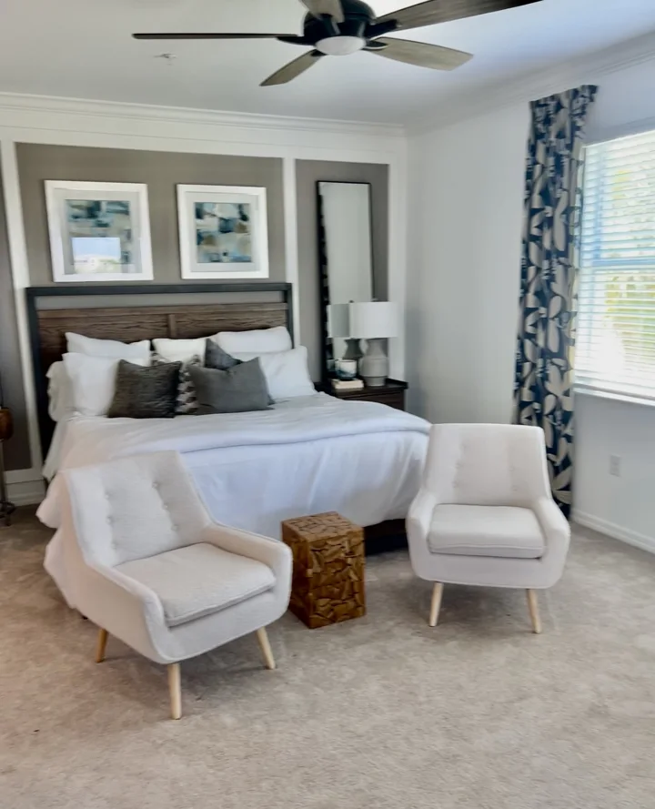 Bedroom with a wood and black headboard, white bedding, and two upholstered chairs